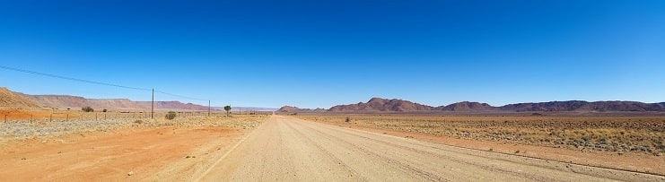 A straight gravel road stretching across the flat Namibian desert toward distant hills.