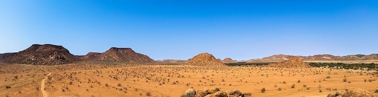 Wide Namibian desert landscape with rocky outcrops and scrubland under a blue sky.