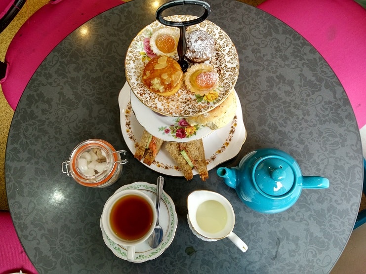 Afternoon tea on a tiered stand with scones and cakes, a blue teapot and cup in Edinburgh