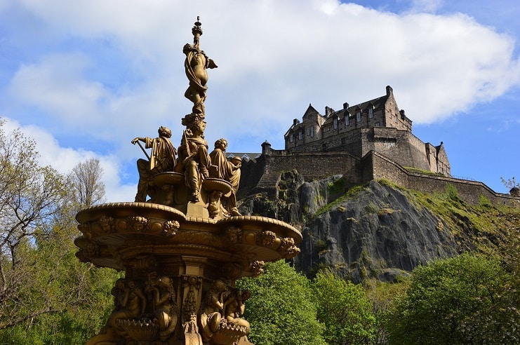 A view of Edinburgh Castle from below in the park with a spectacular fountain in front