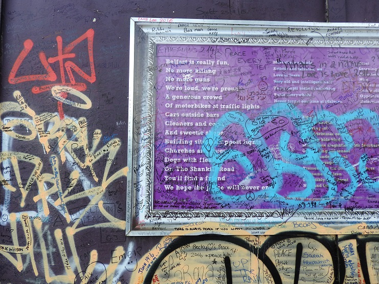 A framed peace poem covered in handwritten messages on a graffiti-covered wall in Belfast.