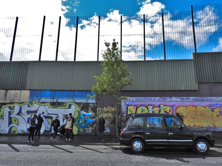 People look at graffiti along Belfast's peace wall as a black taxi passes on the road.