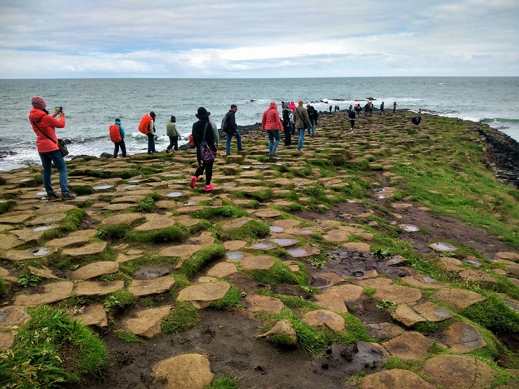 Visitors walk across the hexagonal basalt columns of the Giant's Causeway beside the sea.
