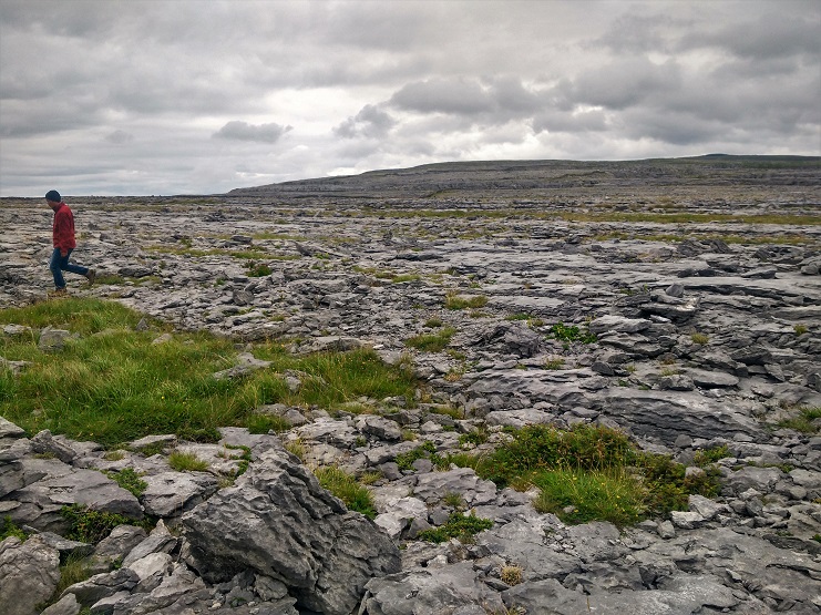 A person in red walks across the bare limestone pavement of the Burren in County Clare, Ireland.