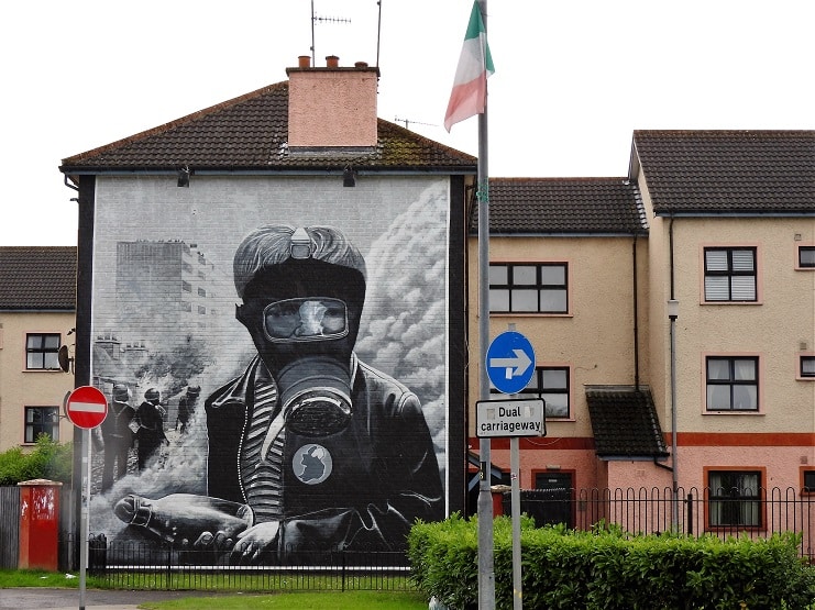 A large gas-mask figure mural on the end of a house in Derry, with an Irish flag flying nearby.