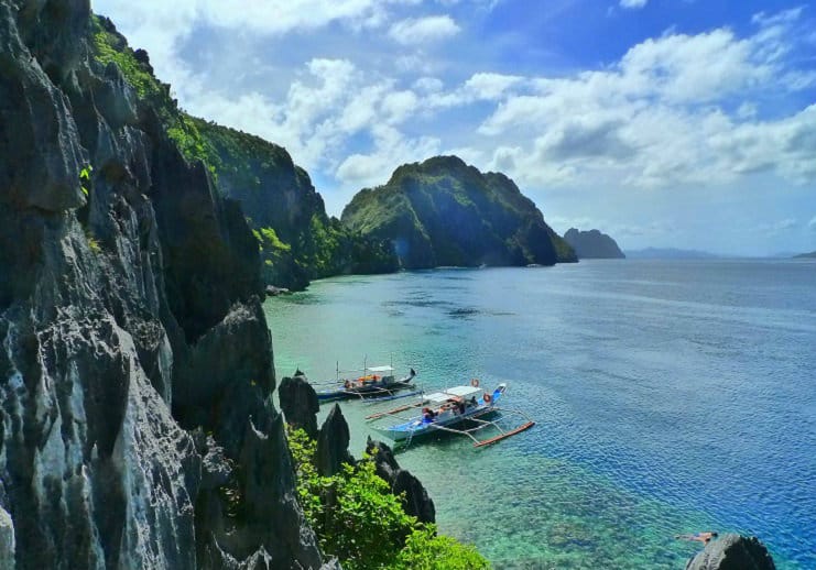 Outrigger boats float in a turquoise lagoon below limestone cliffs in El Nido, Palawan.