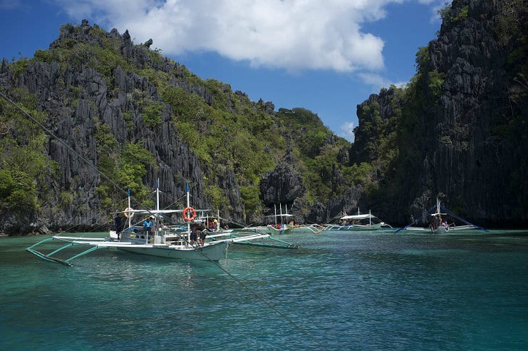 Filipino outrigger boats moored in a clear green lagoon between limestone cliffs in El Nido.