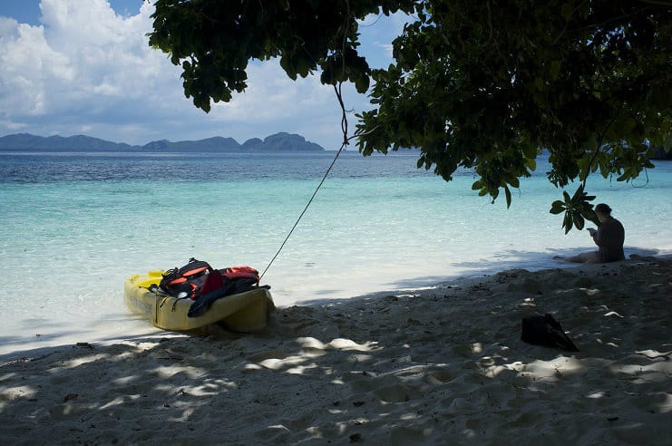 A yellow kayak rests on a white sand beach beside clear turquoise water in Palawan.