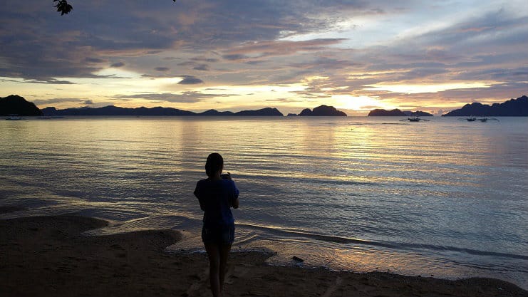 A woman stands silhouetted on the beach watching the sunset over islands in El Nido, Palawan.