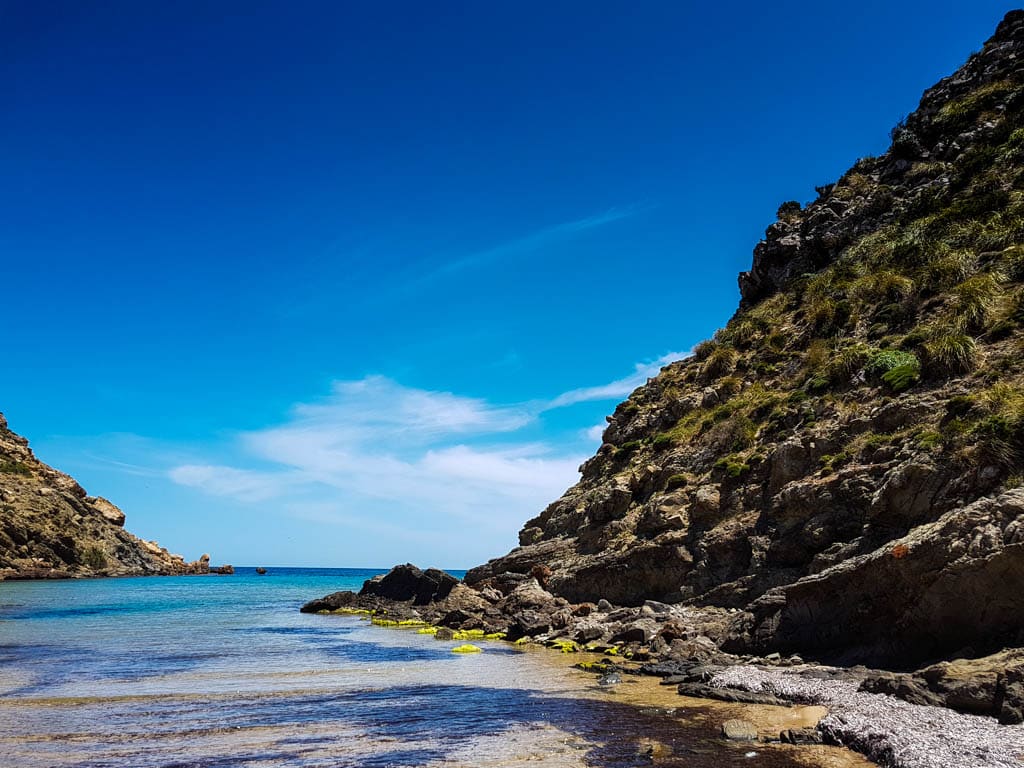 Rocky cove with turquoise water and steep cliffs under a clear blue sky on the Cami de Cavalls, Menorca