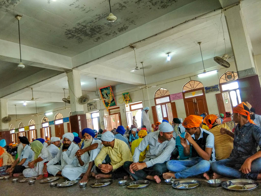 Pilgrims sit in rows on the floor with metal plates at the Golden Temple langar dining hall.