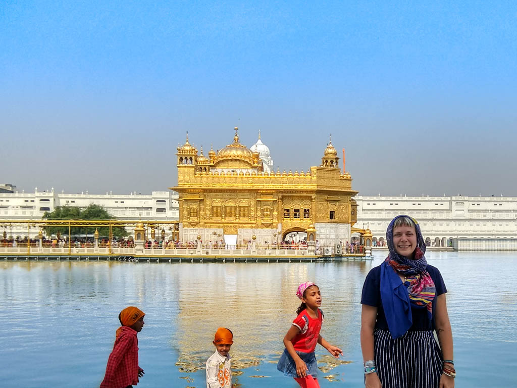 Alice stands by the water of the Golden Temple in Amritsar as children wade nearby.