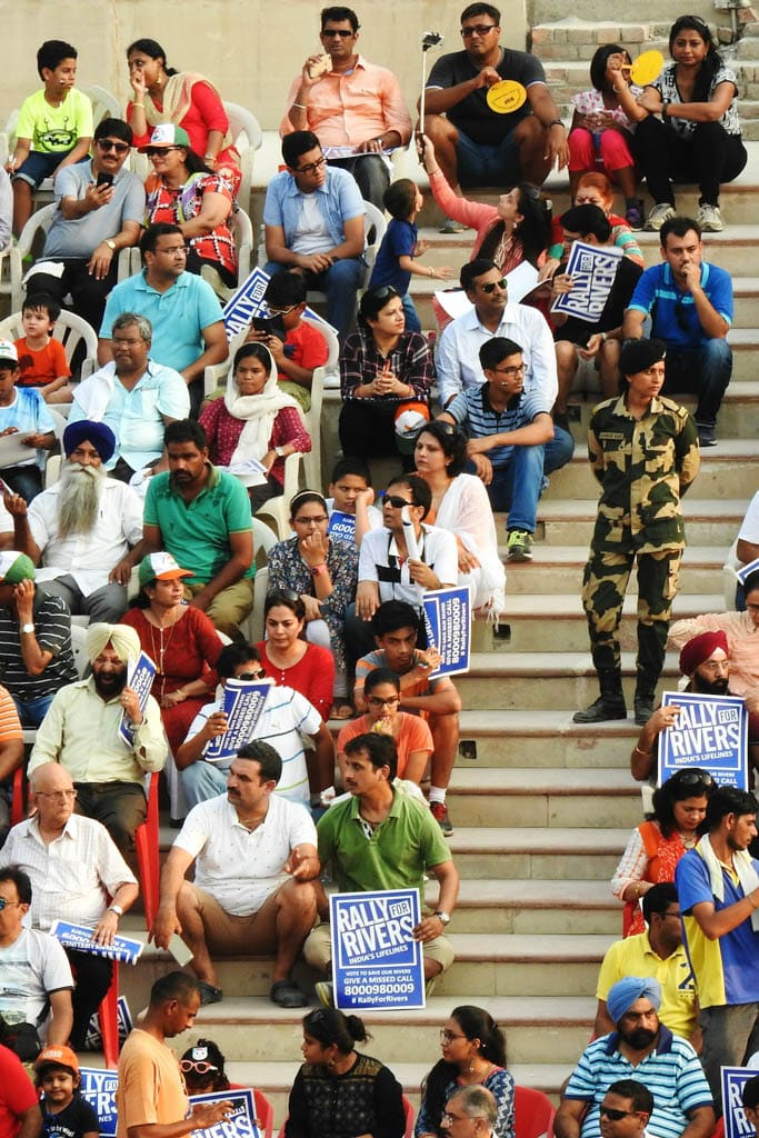 Crowds seated on stadium steps hold 'Rally for Rivers' signs at the Wagah border ceremony.