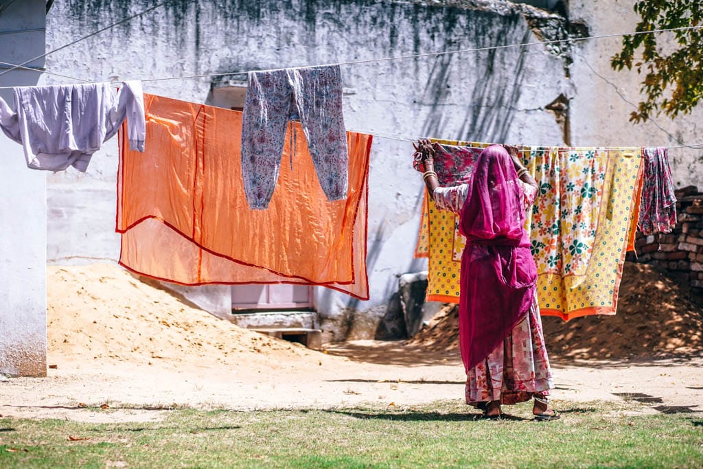 A woman in a pink sari hangs washing on a line outside a village house in India.