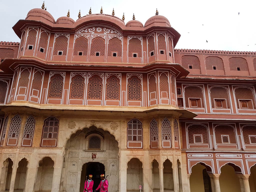 Pink and cream facade of the City Palace in Jaipur with guards in pink beneath the arched entrance.