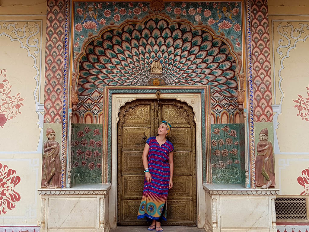 Alice in a striped dress standing in the painted peacock-arch doorway at the City Palace, Jaipur.