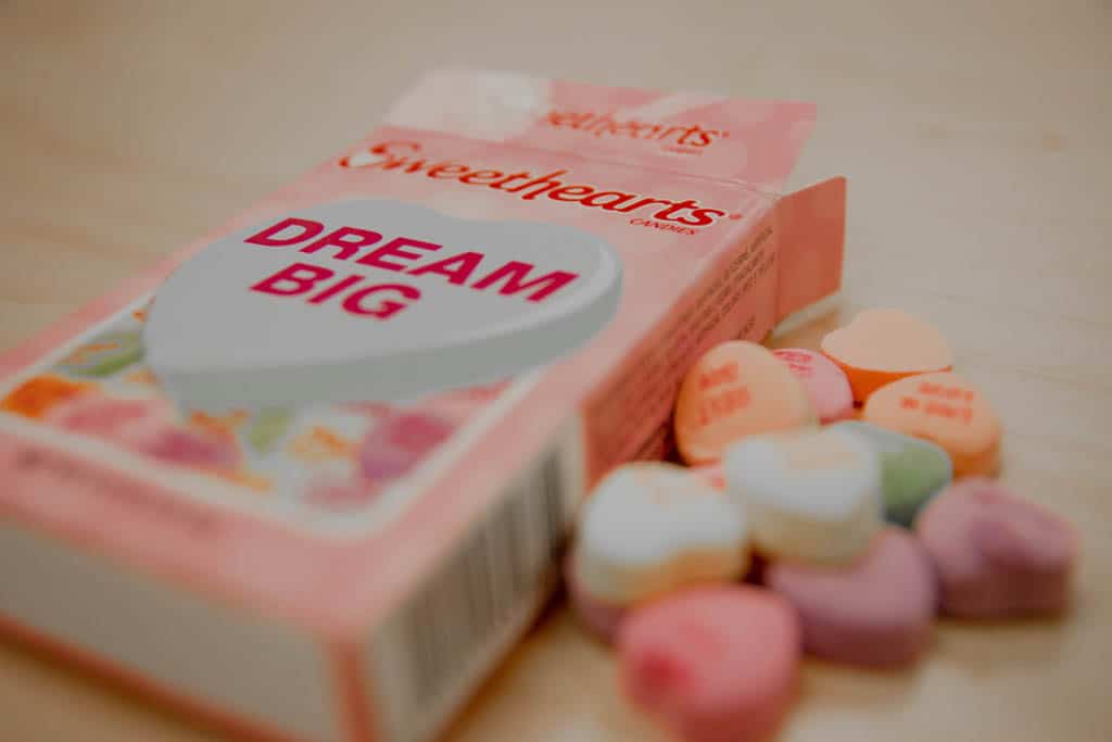 A box of Sweethearts candy reading 'Dream Big' with pastel love heart sweets spilled beside it.