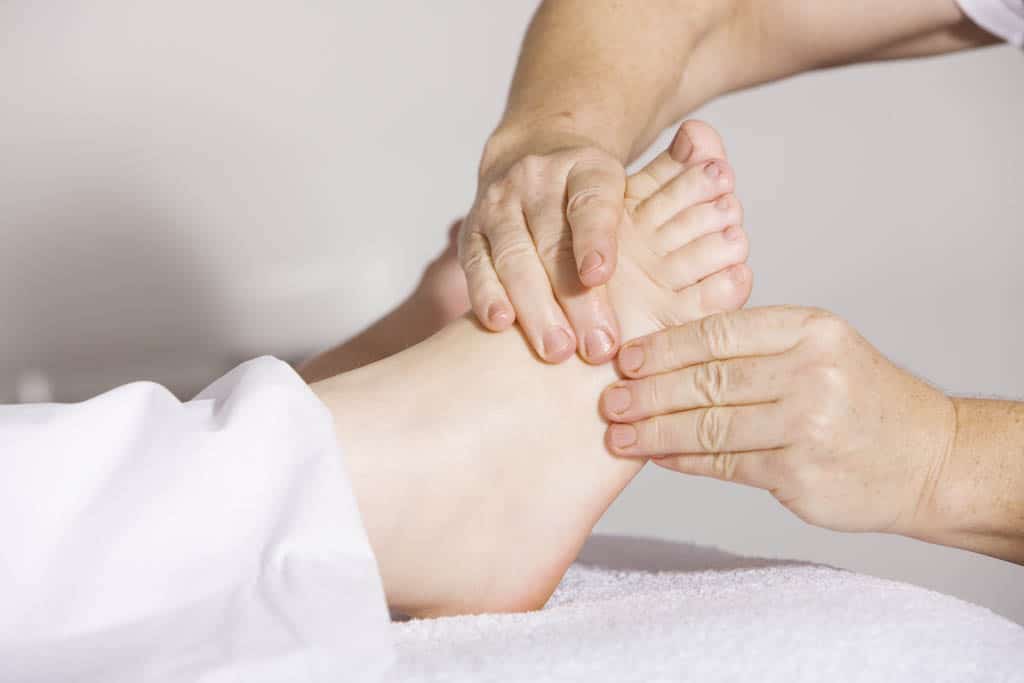 A therapist's hands giving a foot and ankle massage on a white towel.
