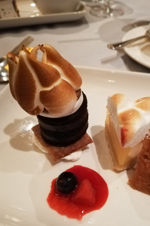 Plated dessert with a toasted meringue-topped chocolate tower, lemon tart slice and fruit coulis.