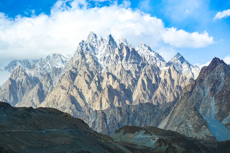 Jagged snow-capped peaks rising above brown foothills along a trek in Pakistan