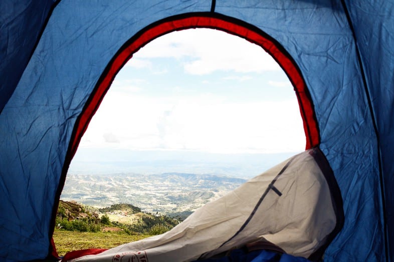 Scene from the inside of a blue tent looking out onto rolling hills and blue skies