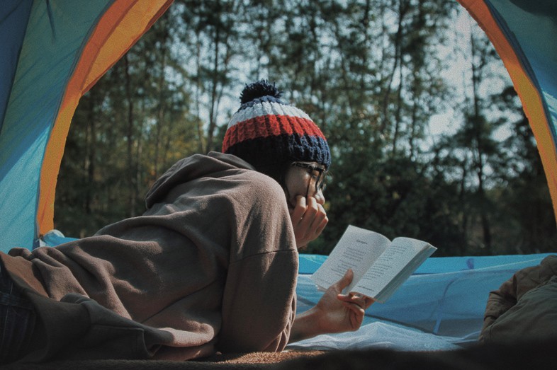 Woman reading a book in her tent in the woods camping alone