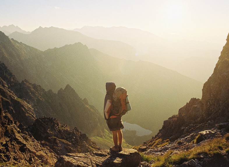 Solo female traveler with a backpack looking out onto a scenery of mountain tops