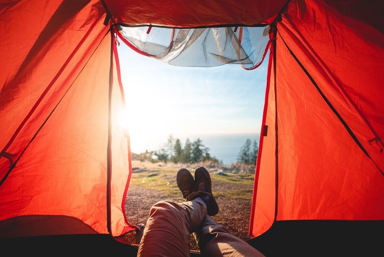 Person lying down in an orange tent looking out onto a countryside scene with the light shining through