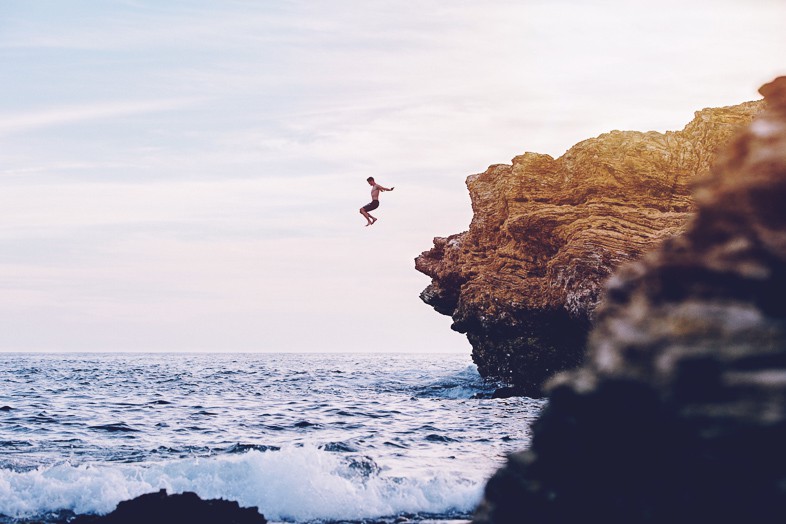 Adventurer jumping from a cliff into the sea