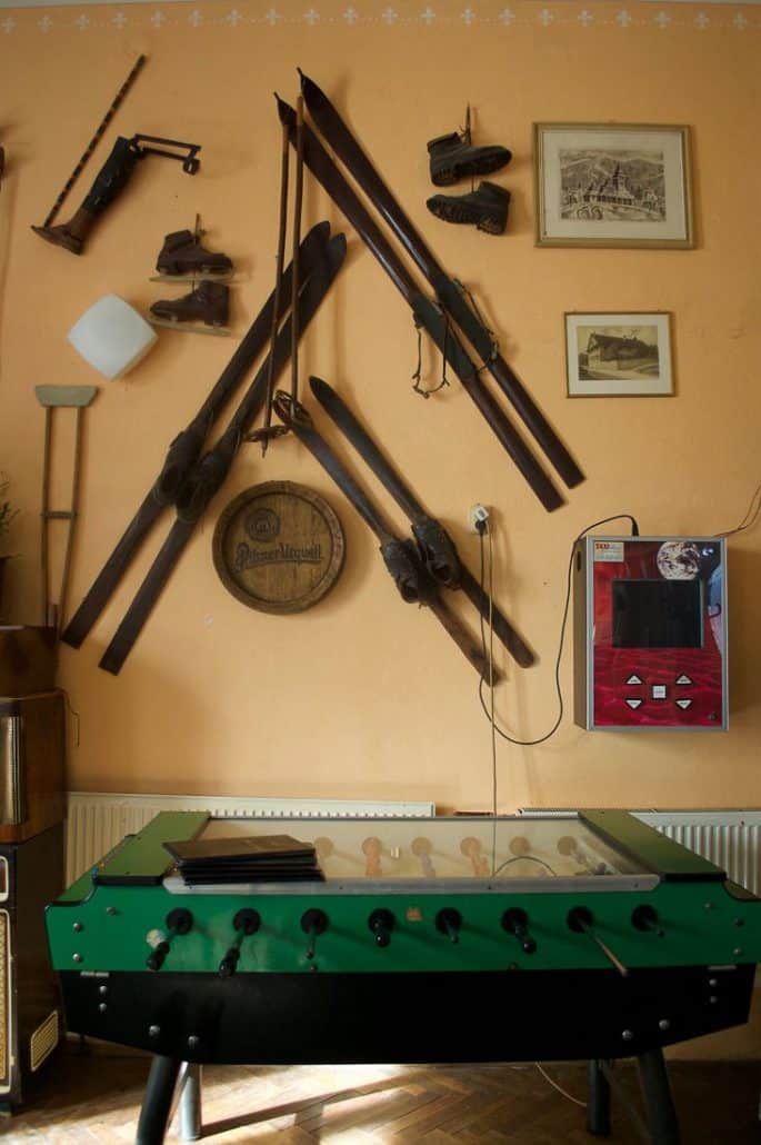 Photo inside a chalet showing some vintage ski equipment that is hung on the wall as well as an old foosball table in front.