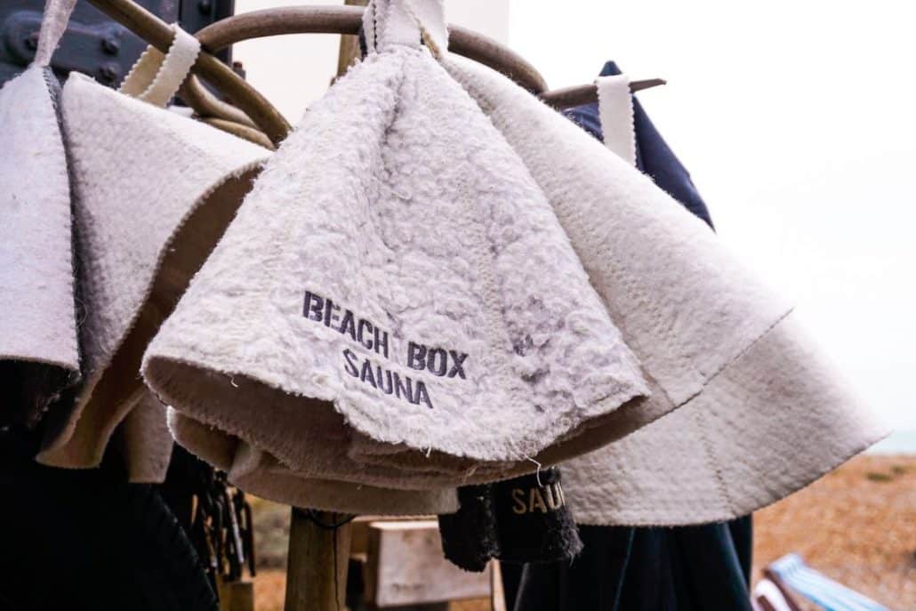Woollen sauna hats hanging on hooks, one stitched 'Beach Box Sauna', on Brighton beach