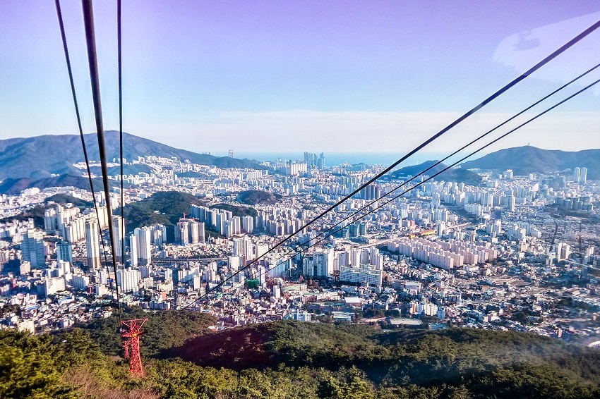 Busan cityscape seen from a cable car on Geumjeongsan Mountain, with the sea beyond the buildings