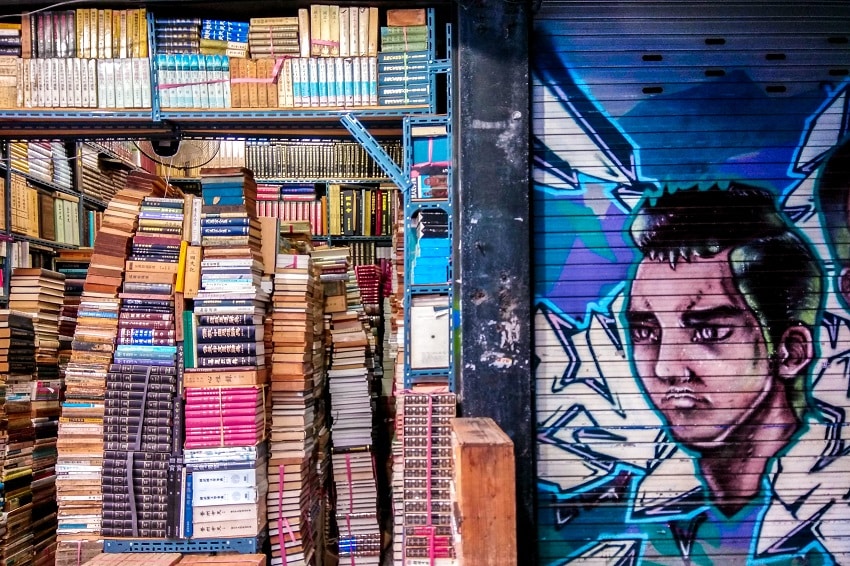 Piles and piles of books next to a shutter with cool street art on it in Bosu-dong Bookstore Alley